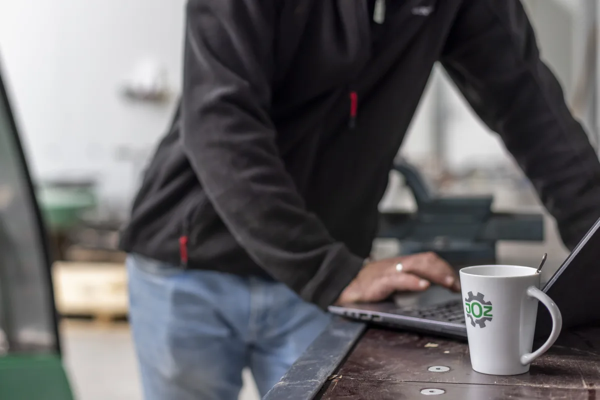 JOZ-Mitarbeiter arbeitet an einem Laptop, im Vordergrund eine weiße Kaffeetasse mit dem JOZ-Logo